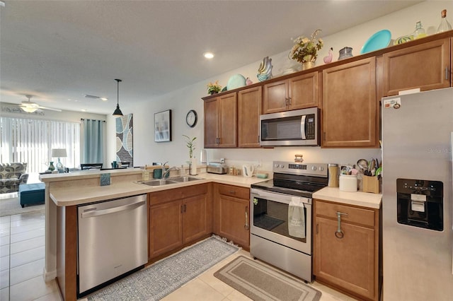 kitchen with brown cabinets, stainless steel appliances, light countertops, a sink, and a peninsula