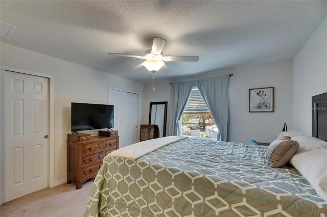 bedroom with light carpet, ceiling fan, a textured ceiling, and two closets