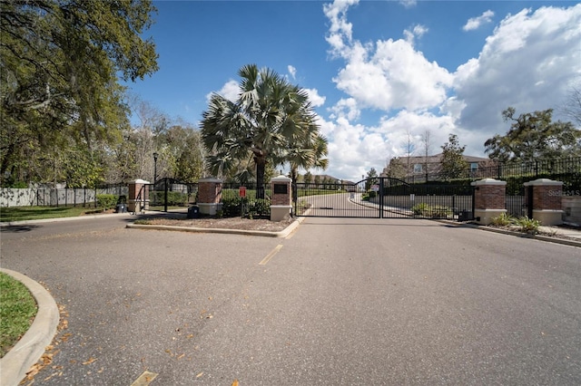 view of asphalt street with a gate, curbs, and a gated entry