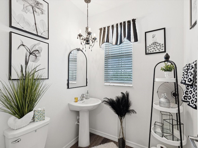 half bathroom featuring a chandelier, baseboards, toilet, and wood finished floors