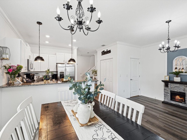 dining space featuring a stone fireplace, ornamental molding, dark wood finished floors, and an inviting chandelier