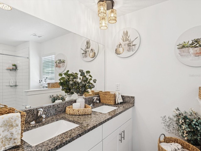 full bath featuring tiled shower, a sink, an inviting chandelier, and double vanity