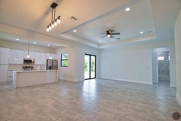9 Tee View Rd, Rotonda West, FL 33947 - unfurnished living room featuring a tray ceiling, ceiling fan, and recessed lighting