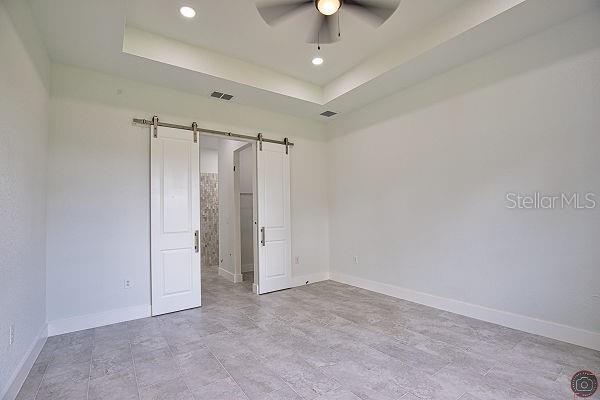 9 Tee View Rd, Rotonda West, FL 33947 - spare room featuring a barn door, ceiling fan, a tray ceiling, and recessed lighting