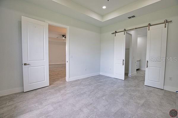 9 Tee View Rd, Rotonda West, FL 33947 - unfurnished bedroom with a barn door, a raised ceiling, and recessed lighting