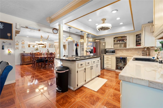 kitchen with beverage cooler, a raised ceiling, appliances with stainless steel finishes, a sink, and backsplash