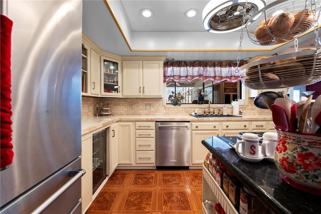 kitchen featuring stainless steel appliances, decorative backsplash, cream cabinets, glass insert cabinets, and a sink