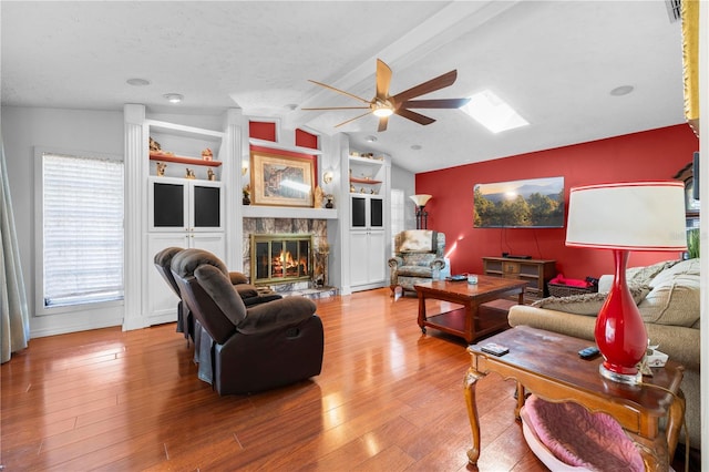 living room featuring wood-type flooring, ceiling fan, a stone fireplace, and lofted ceiling with beams