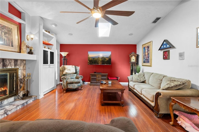 living room featuring built in features, visible vents, wood finished floors, vaulted ceiling, and a fireplace