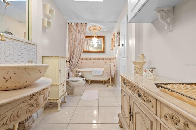 full bath featuring a wainscoted wall, tile patterned flooring, a freestanding bath, a textured ceiling, and tile walls