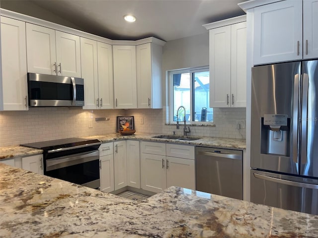 kitchen with a sink, appliances with stainless steel finishes, white cabinets, decorative backsplash, and light stone countertops