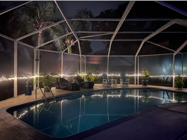 pool at night with a patio area, glass enclosure, and an outdoor pool