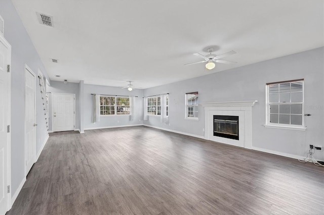 unfurnished living room with visible vents, baseboards, a ceiling fan, dark wood-style floors, and a glass covered fireplace