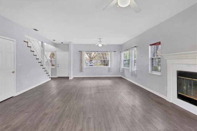 unfurnished living room with ceiling fan, a tile fireplace, wood finished floors, baseboards, and stairway