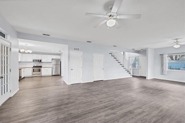 unfurnished living room featuring stairs, visible vents, dark wood-type flooring, baseboards, and ceiling fan with notable chandelier