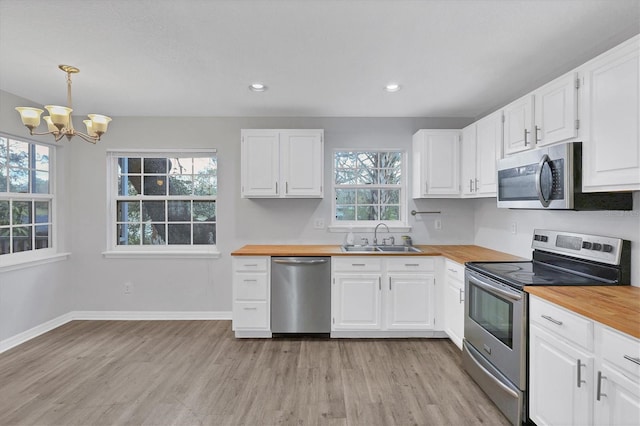 kitchen with baseboards, appliances with stainless steel finishes, white cabinetry, wooden counters, and a sink