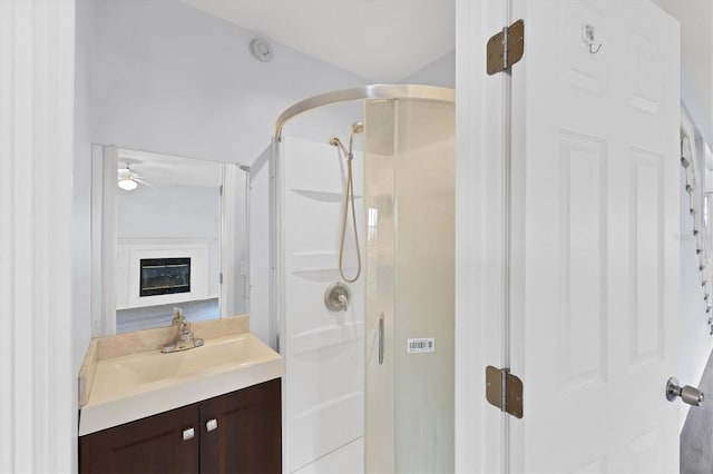 full bath featuring a stall shower, ceiling fan, a glass covered fireplace, and vanity