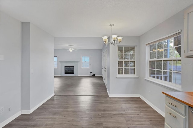 unfurnished dining area featuring ceiling fan with notable chandelier, baseboards, wood finished floors, and a glass covered fireplace