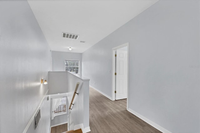 corridor with baseboards, visible vents, wood finished floors, and an upstairs landing