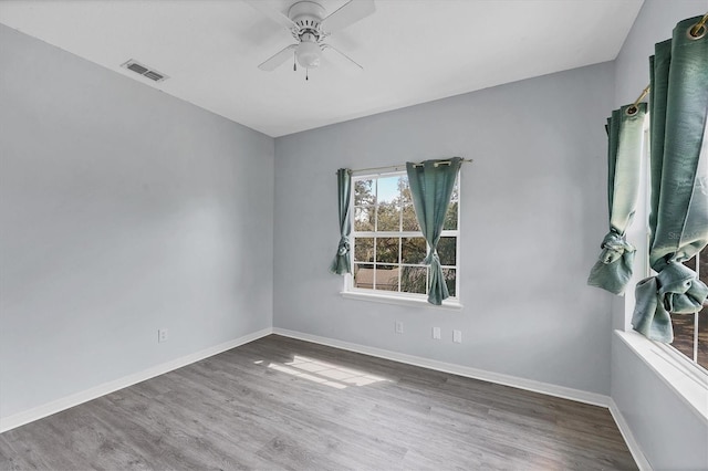 empty room with a ceiling fan, wood finished floors, visible vents, and baseboards