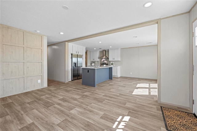 kitchen featuring light wood finished floors, stainless steel fridge with ice dispenser, wall chimney exhaust hood, open floor plan, and light countertops