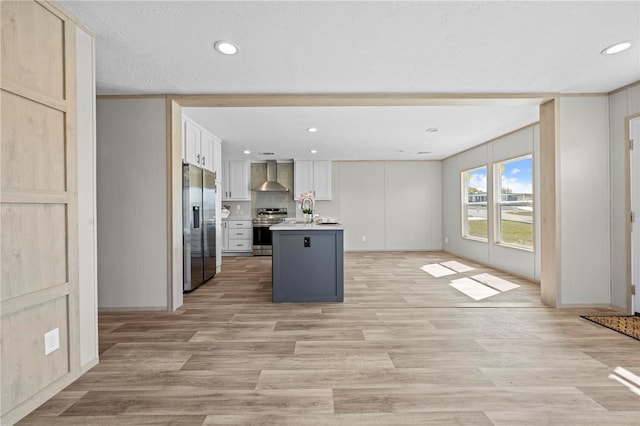 kitchen with light countertops, appliances with stainless steel finishes, open floor plan, a sink, and wall chimney exhaust hood