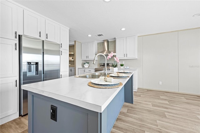 kitchen with light countertops, white cabinets, stainless steel fridge, and wall chimney exhaust hood