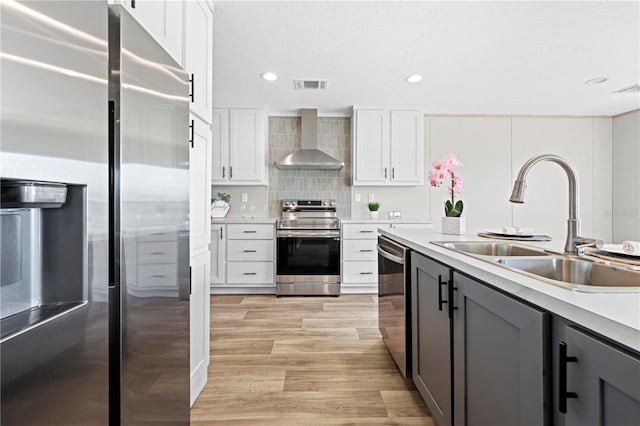 kitchen with a sink, visible vents, light countertops, wall chimney range hood, and appliances with stainless steel finishes