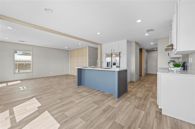 kitchen with light wood-style floors, stainless steel fridge, range hood, and light countertops