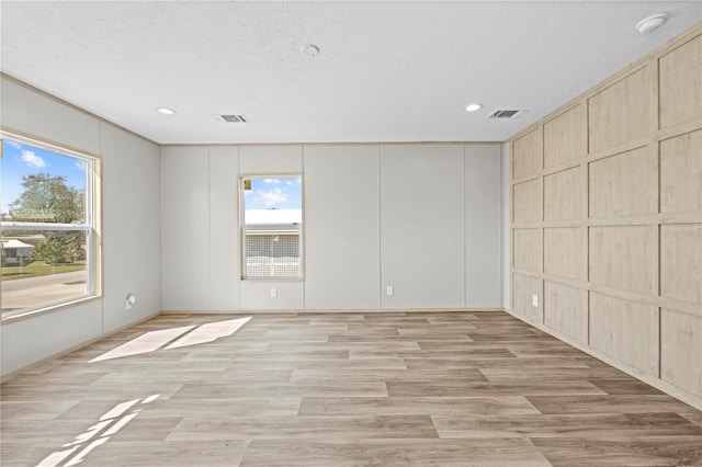 spare room with light wood-type flooring, visible vents, and a decorative wall