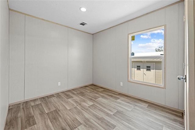 spare room featuring light wood finished floors, visible vents, and a decorative wall