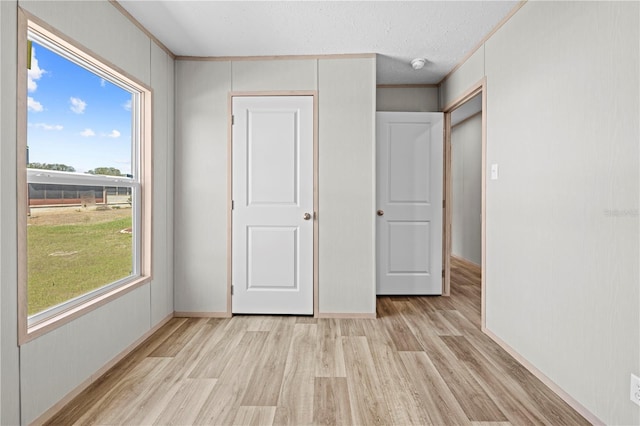 unfurnished bedroom featuring light wood-style floors, ornamental molding, and a textured ceiling