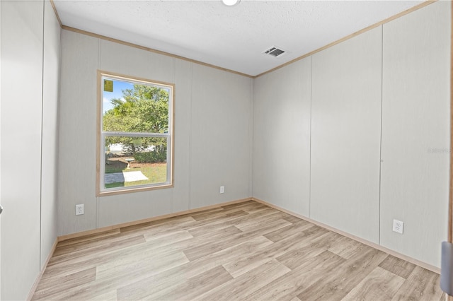 unfurnished room with light wood finished floors, visible vents, a decorative wall, and a textured ceiling