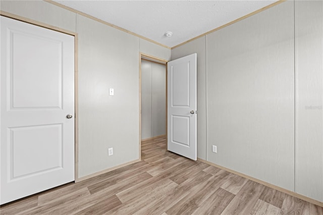 unfurnished bedroom featuring light wood-type flooring, a closet, crown molding, and a textured ceiling