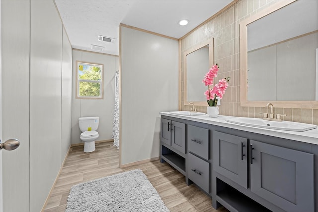 bathroom with toilet, double vanity, a sink, and wood finished floors