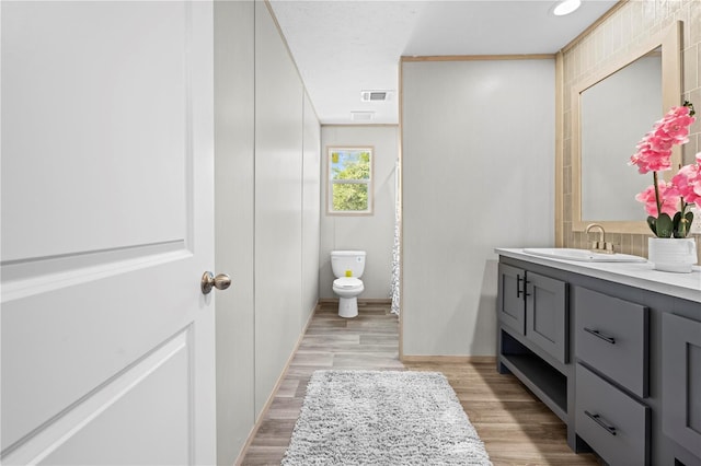 bathroom with toilet, wood finished floors, vanity, visible vents, and baseboards