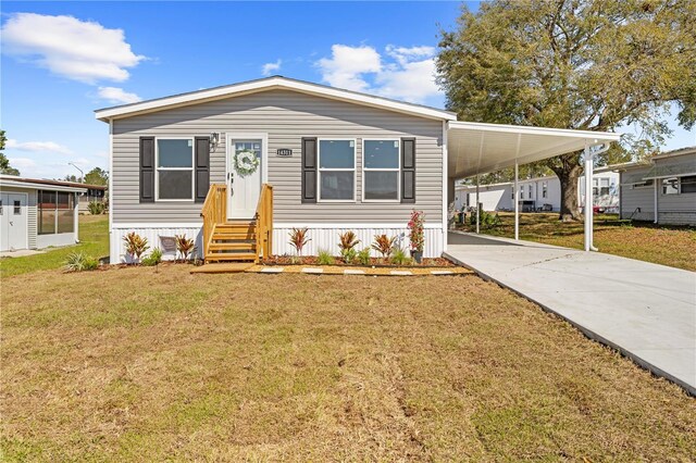 manufactured / mobile home featuring entry steps, a carport, a front lawn, and concrete driveway