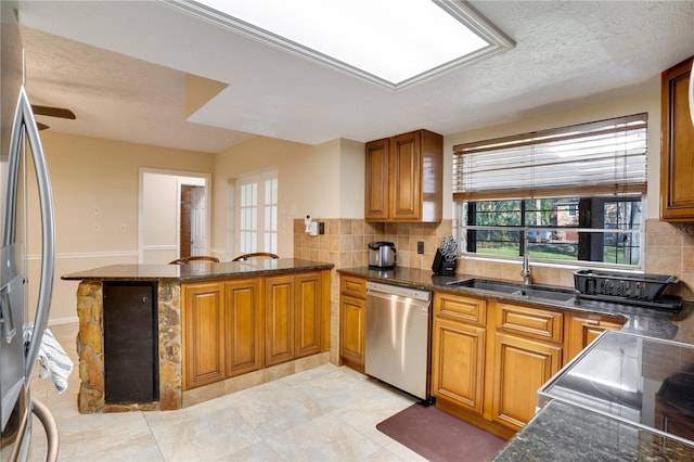 kitchen featuring tasteful backsplash, brown cabinetry, a peninsula, stainless steel appliances, and a sink