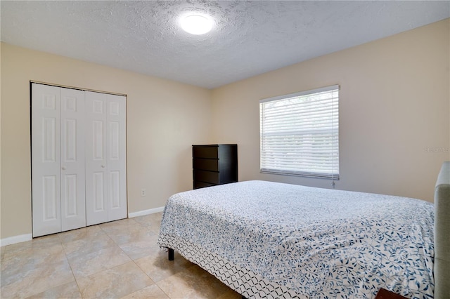 bedroom featuring a closet, a textured ceiling, baseboards, and light tile patterned floors