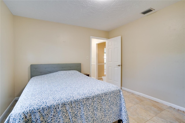 bedroom featuring a textured ceiling, light tile patterned floors, visible vents, and baseboards