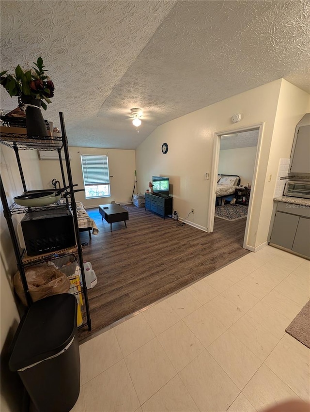 interior space featuring light wood finished floors, vaulted ceiling, a textured ceiling, ceiling fan, and baseboards