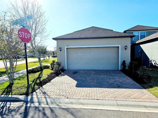 view of front of property featuring roof with shingles, decorative driveway, an attached garage, and stucco siding