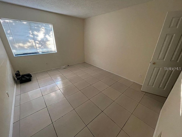 empty room with a textured ceiling and light tile patterned floors