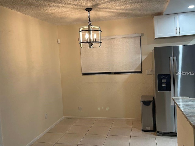 unfurnished dining area with light tile patterned floors, baseboards, a textured ceiling, and an inviting chandelier