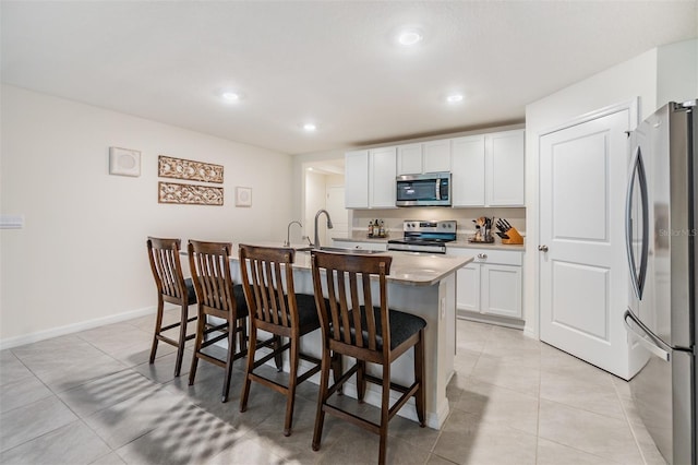 kitchen with appliances with stainless steel finishes, white cabinetry, an island with sink, and a kitchen bar