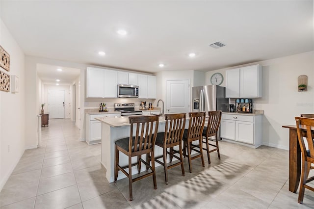 kitchen with visible vents, appliances with stainless steel finishes, a kitchen breakfast bar, a kitchen island with sink, and light countertops