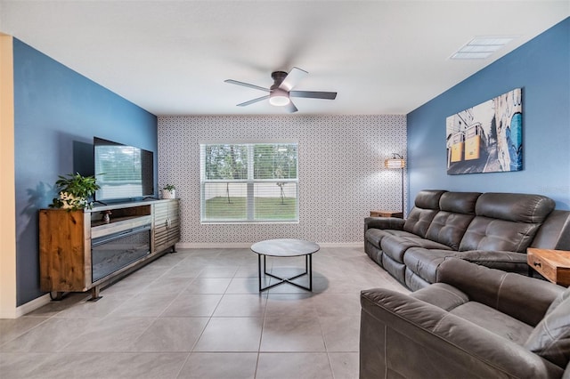 living area featuring ceiling fan, an accent wall, visible vents, baseboards, and wallpapered walls