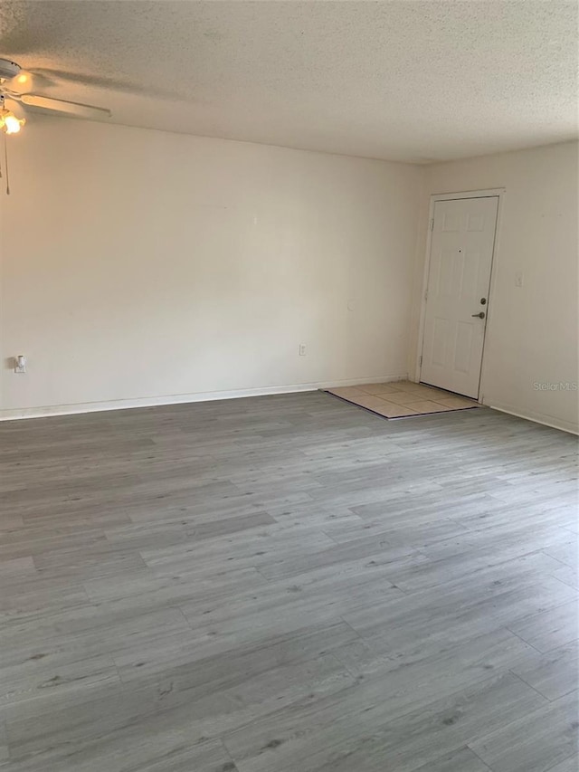 spare room featuring a textured ceiling, wood finished floors, baseboards, and ceiling fan