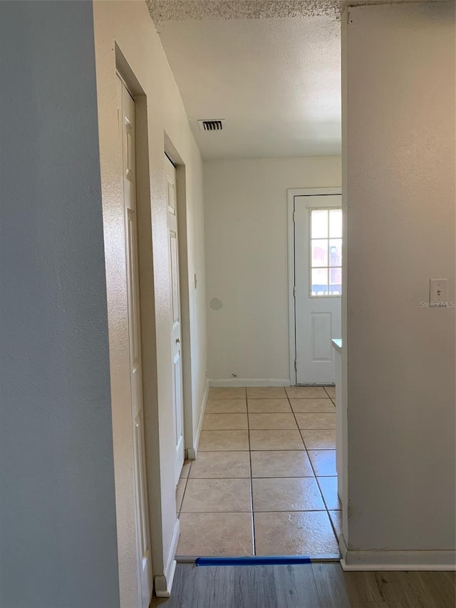 hallway featuring tile patterned floors, visible vents, baseboards, and a textured ceiling