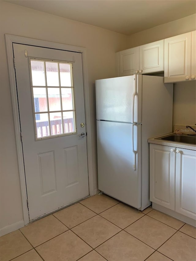 kitchen featuring white cabinetry, light tile patterned floors, freestanding refrigerator, and a sink